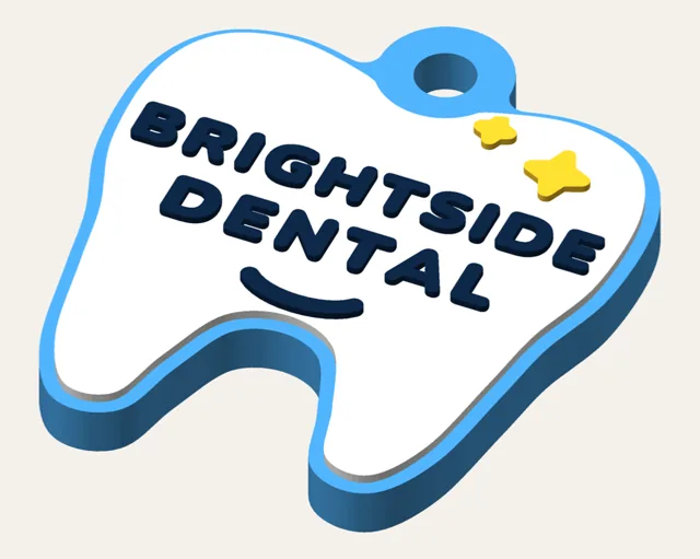 Glossy white molar keychain on a blue backing, with yellow sparkles, a smile and BRIGHTSIDE DENTAL in navy.