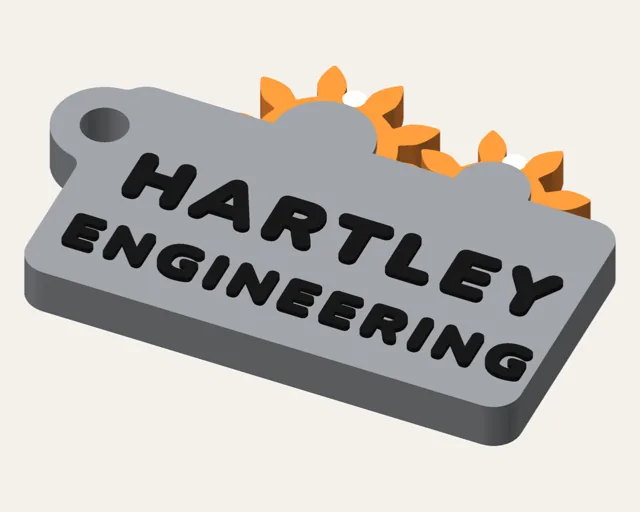 Grey keychain with the top halves of two orange gears peeking out above a cover, and HARTLEY ENGINEERING in black.